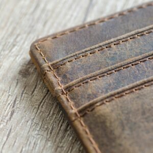 Detailed shot of a brown leather wallet on a textured wooden surface, showcasing stitching.